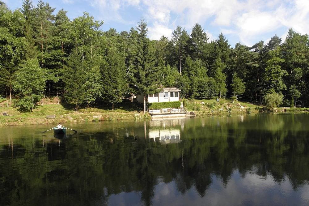 Foto 12 von 21: Chalet mit Blick auf einen Teich in einer grünen Umgebung.